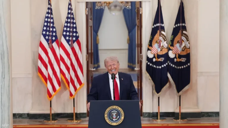 Man in a dark suit and red tie speaks at a podium with the presidential seal, flanked by American and presidential flags.
