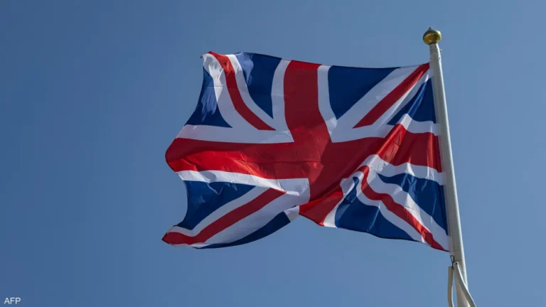 Union Jack flag waving on a flagpole against a clear blue sky, outdoors.