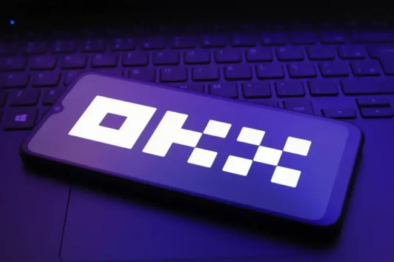 Smartphone resting on a laptop keyboard with a white pixelated 'OK' displayed on the screen against a purple glow.